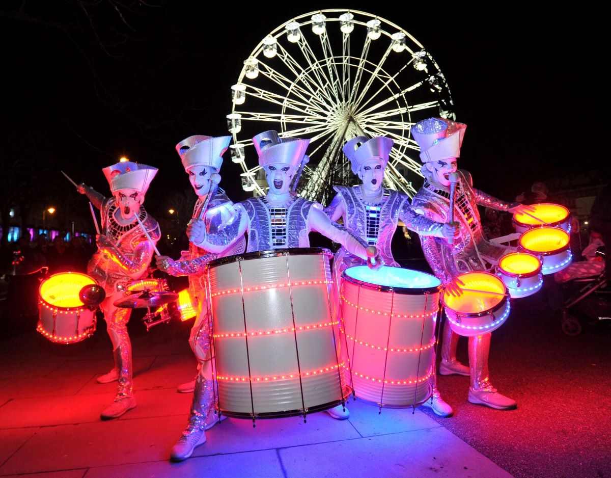 Spark! drumming performers in front of illuminated giant wheel 
